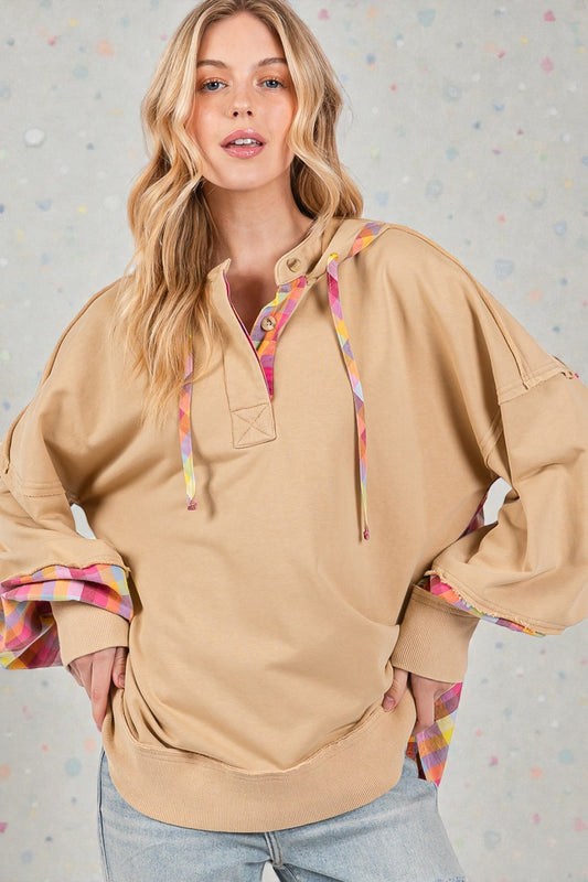 Woman wearing a beige hoodie with colorful accents against a light gray background