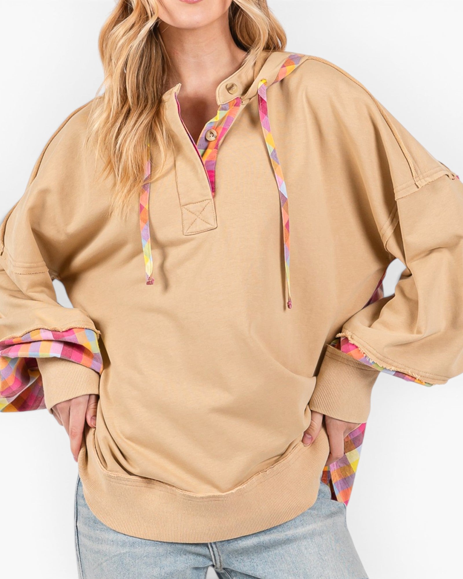 A woman wearing an oversized tan pullover hoodie with colorful tie-dye drawstrings and matching multicolor patterned inner cuffs, paired with light blue jeans against a plain white background.