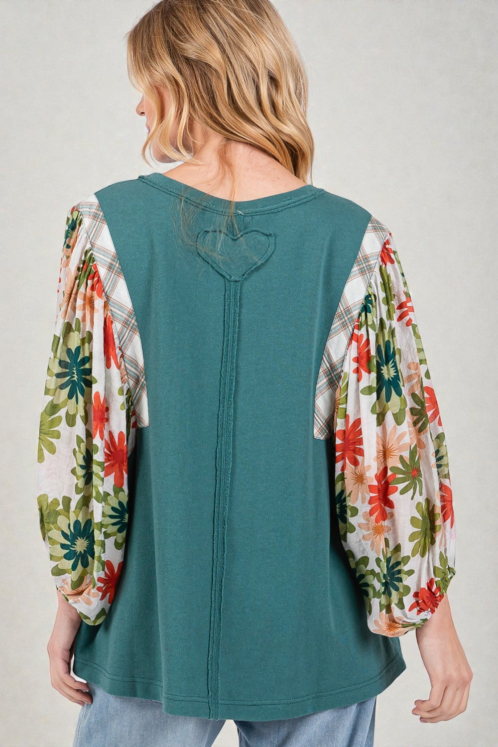 Woman wearing a teal top with floral sleeves on a plain background