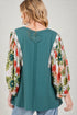 Woman wearing a teal top with floral sleeves on a plain background