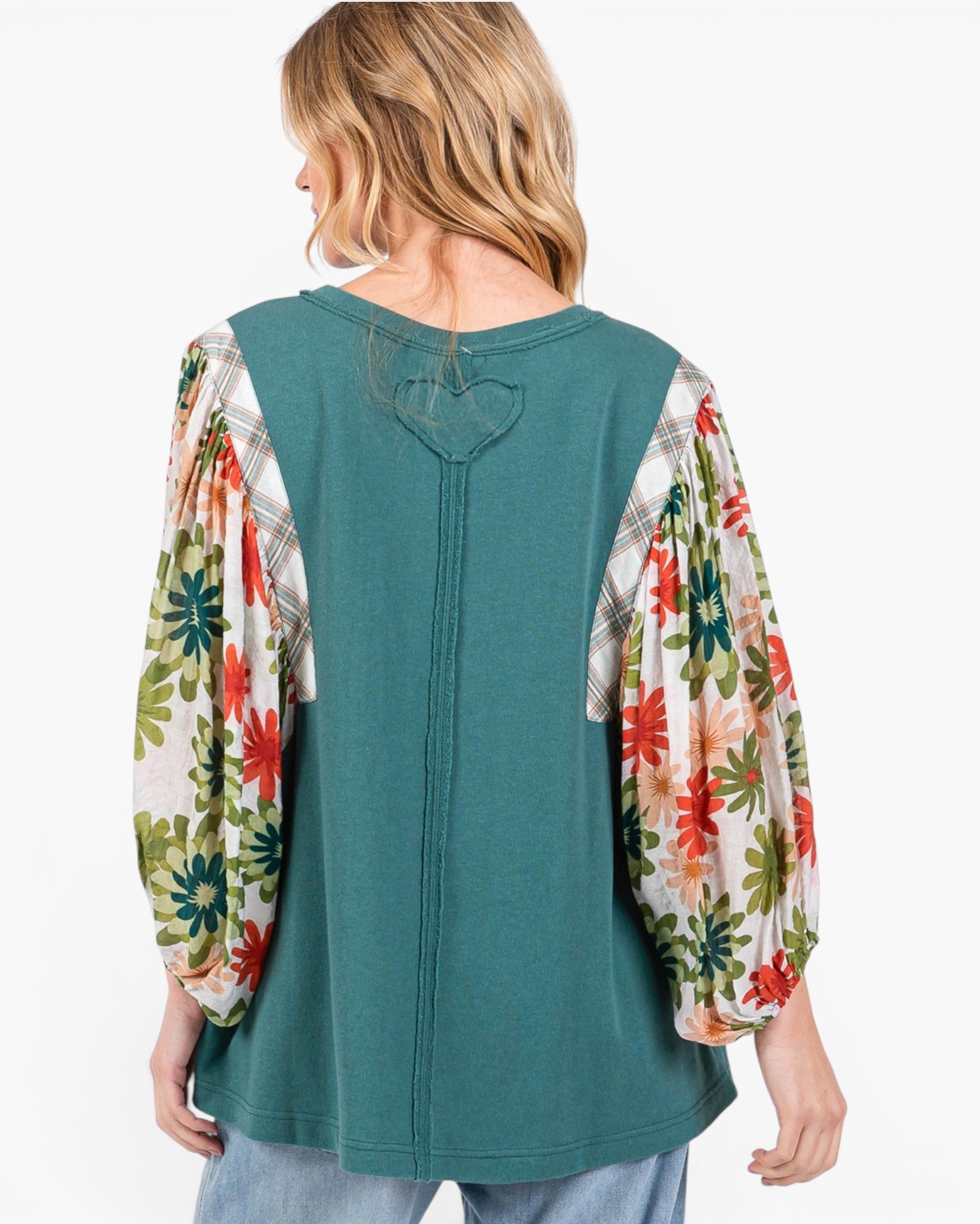 A woman shown from the back wearing a teal long-sleeve top with floral and plaid puff sleeves, paired with light blue jeans, against a plain white background.
