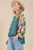 Woman wearing a teal top with floral sleeves and a beige hat against a beige background