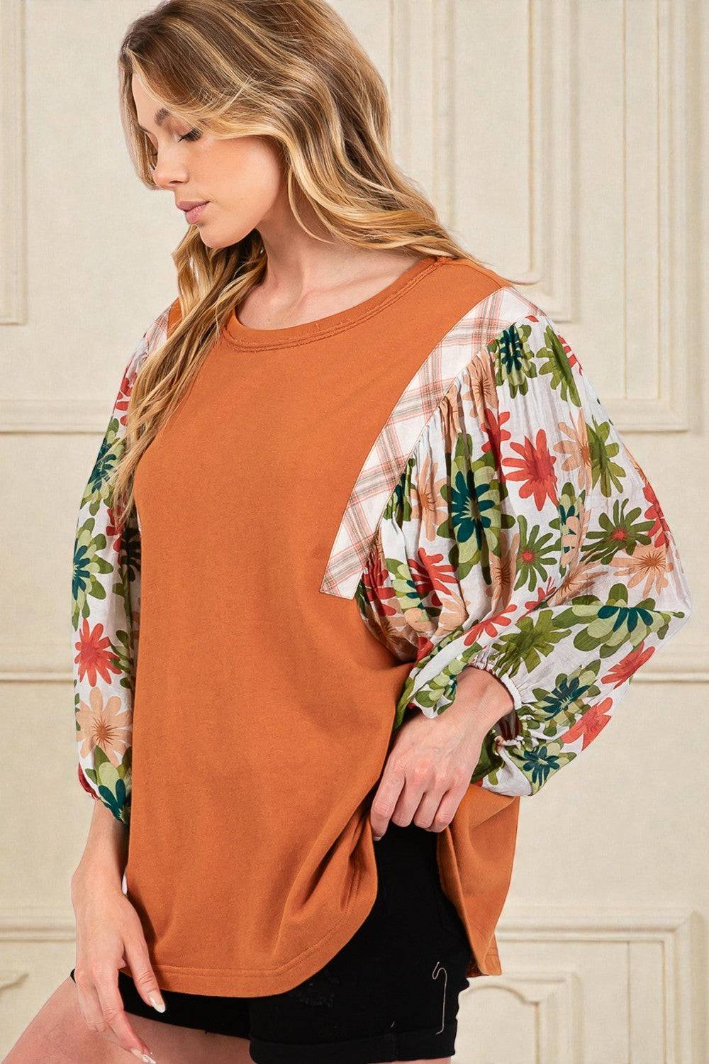 Woman wearing a rust-colored top with floral sleeves against a neutral background