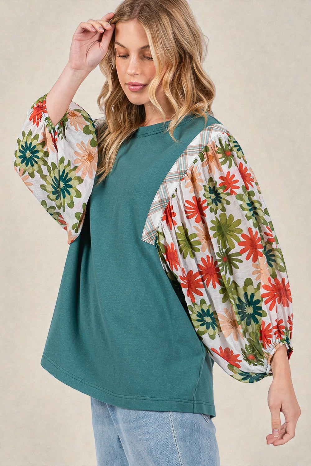 Woman wearing a teal top with floral sleeves against a beige background