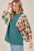 Woman wearing a teal top with floral sleeves against a beige background