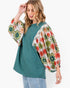 A woman wearing a teal raglan-style top with dramatic floral puff sleeves in red, green, and cream, paired with light blue jeans against a plain white background.