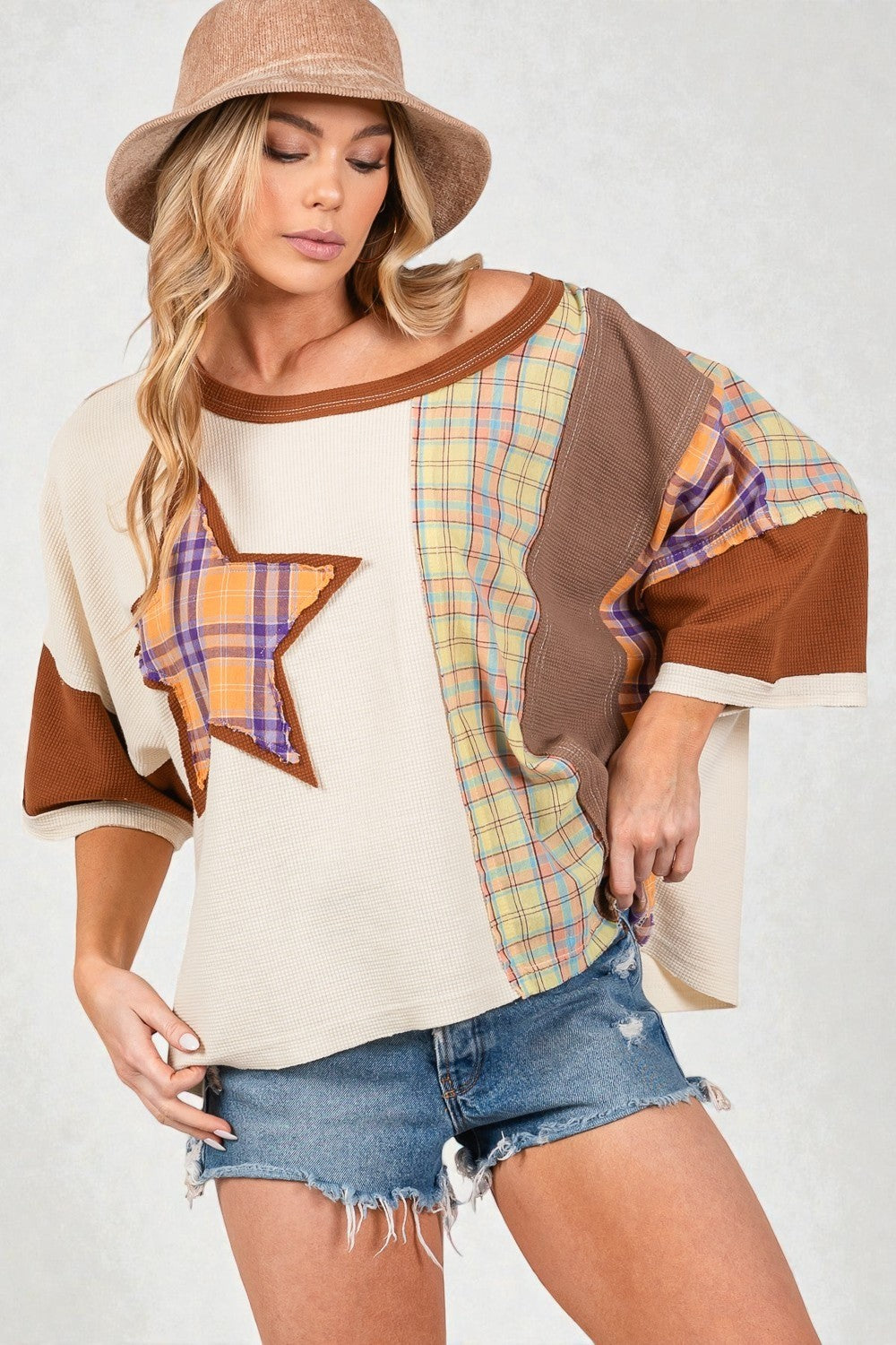 Woman wearing a plaid and brown top with denim shorts on a white background