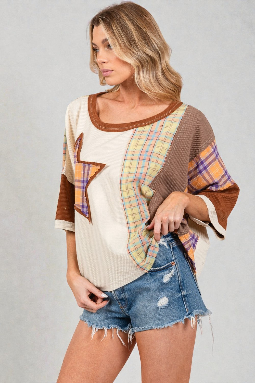 Woman wearing a plaid and brown top with denim shorts on a gray background