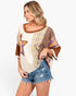 A woman modeling a bohemian-style patchwork top with brown, beige, and plaid patterns, paired with distressed denim shorts against a plain white background.