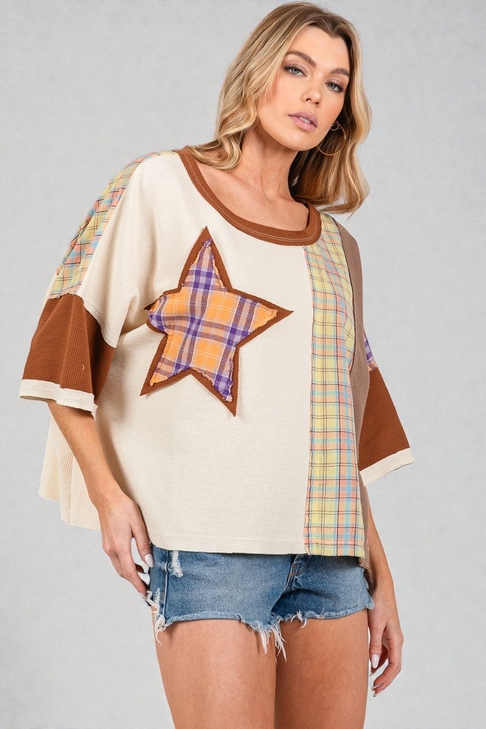Woman wearing a cream-colored top with plaid star and sleeve designs on a gray background