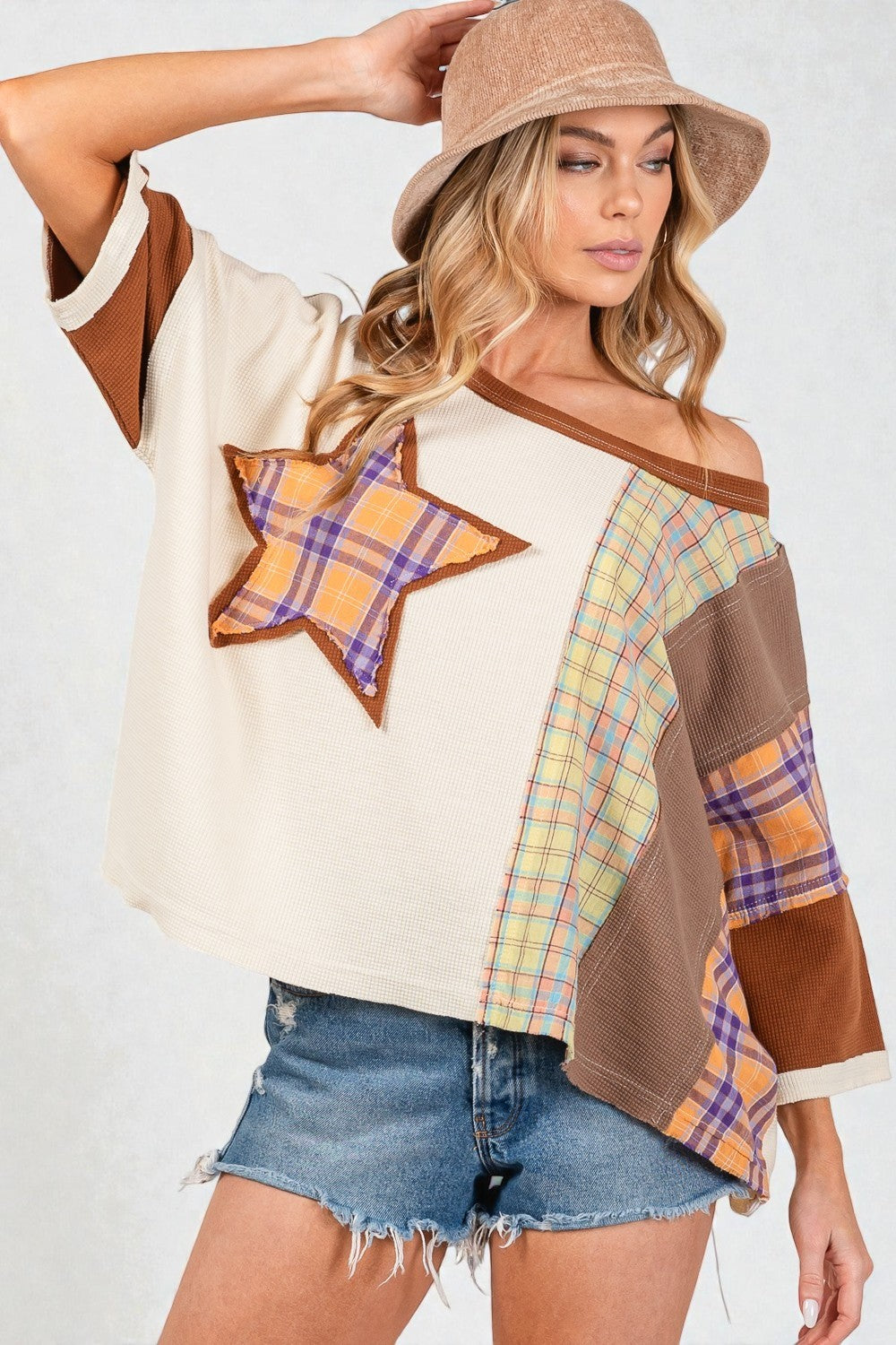 Woman wearing a patchwork top with star design and denim shorts on a white background