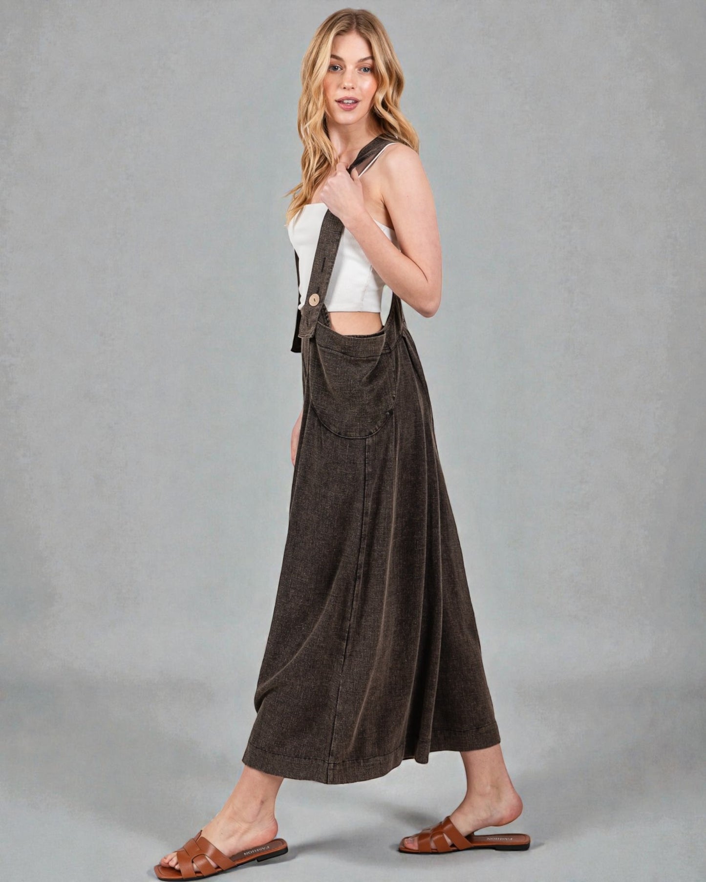 Woman wearing a white top and brown overalls against a gray background