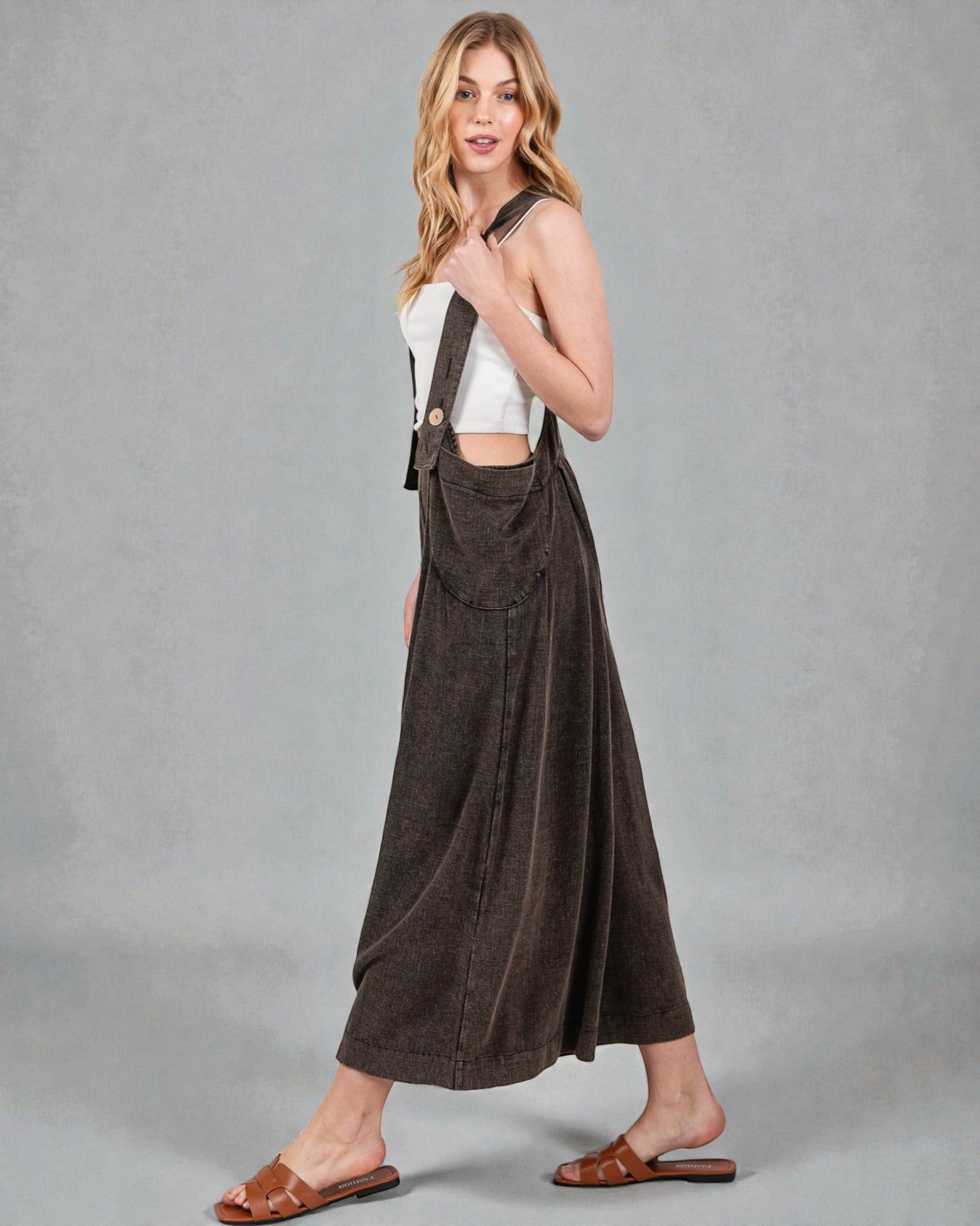 Woman wearing a white top and brown overalls against a gray background