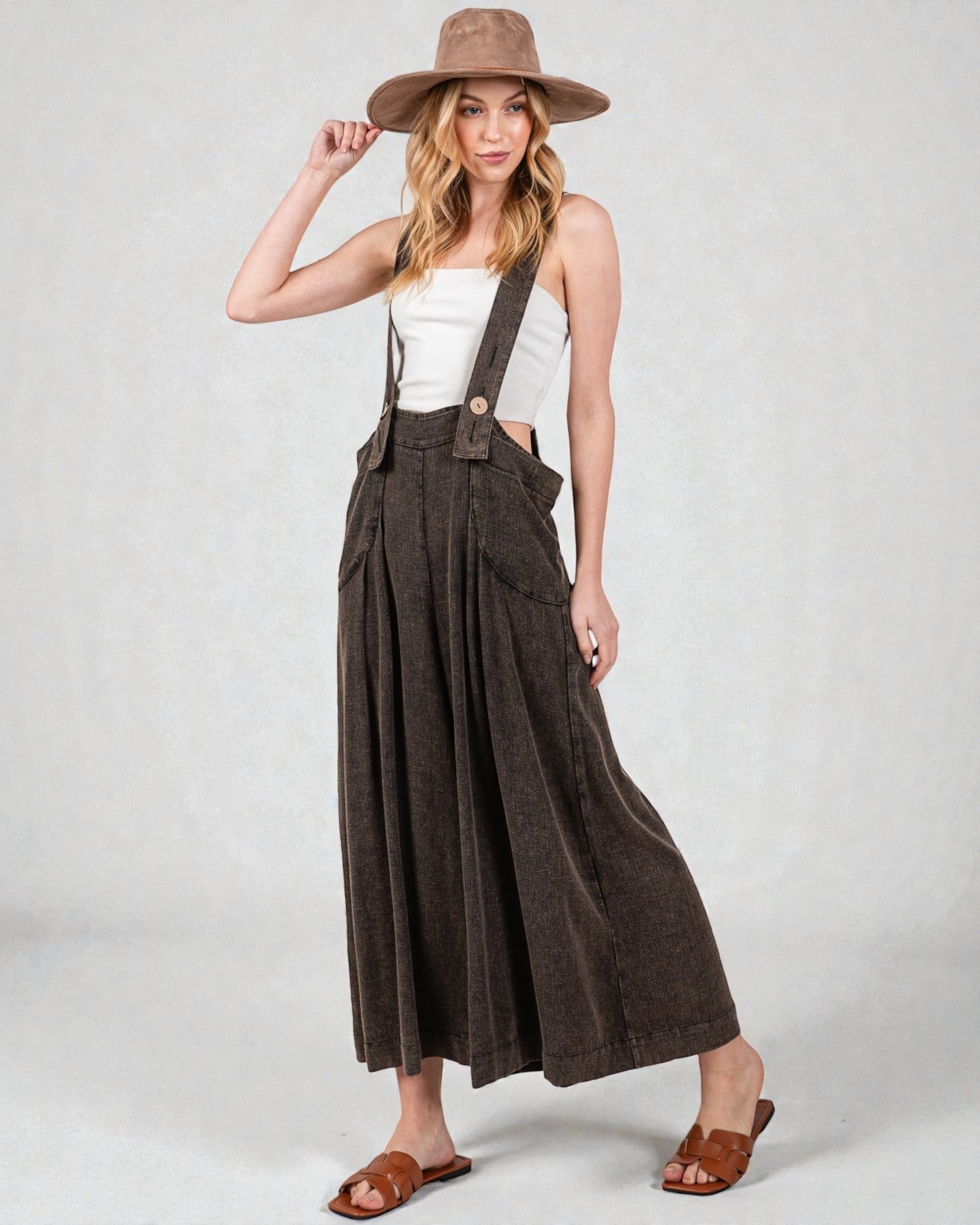 Woman wearing brown wide-leg pants with suspenders and a matching hat on a white background