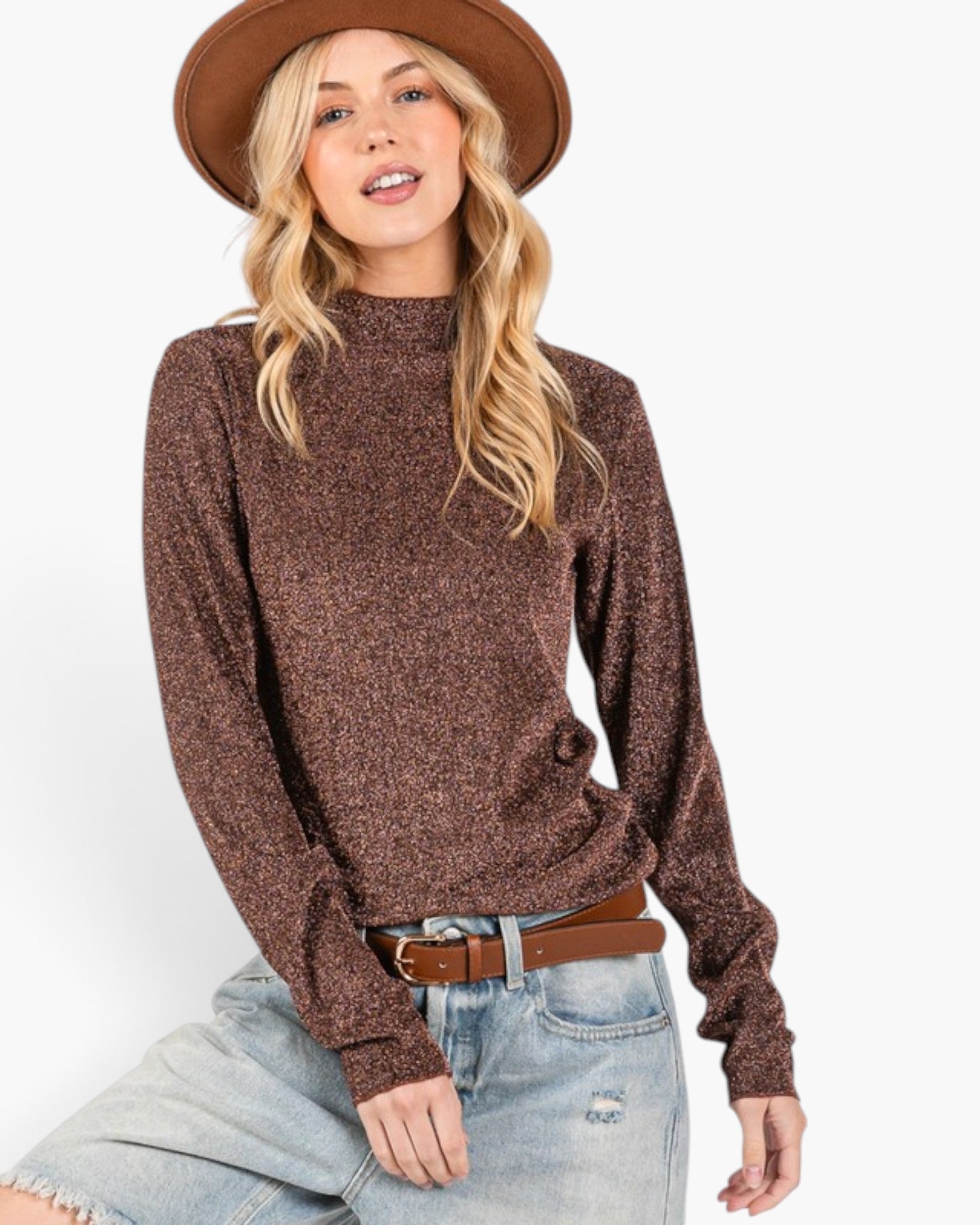 A woman wearing a brown textured knit mock neck sweater, a brown wide-brim hat, and light-wash blue jeans with a brown belt, posed against a solid white background.