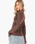 A woman wearing a brown textured knit sweater with a high mock neck and long sleeves, paired with light blue jeans, shown from a three-quarters back view against a plain white background.