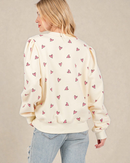 Woman wearing a cream sweater with pink heart patterns on a beige background