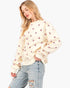 A woman wearing a cream-colored crewneck sweatshirt with a small pink heart pattern, paired with light-wash distressed jeans, against a plain white background.