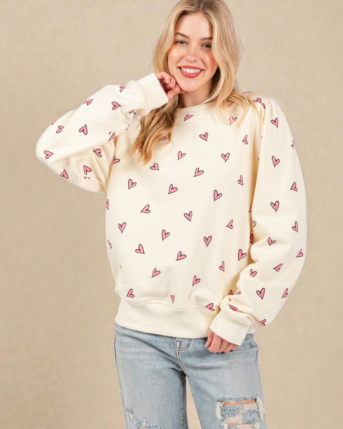 Woman wearing a cream sweatshirt with heart patterns on a beige background