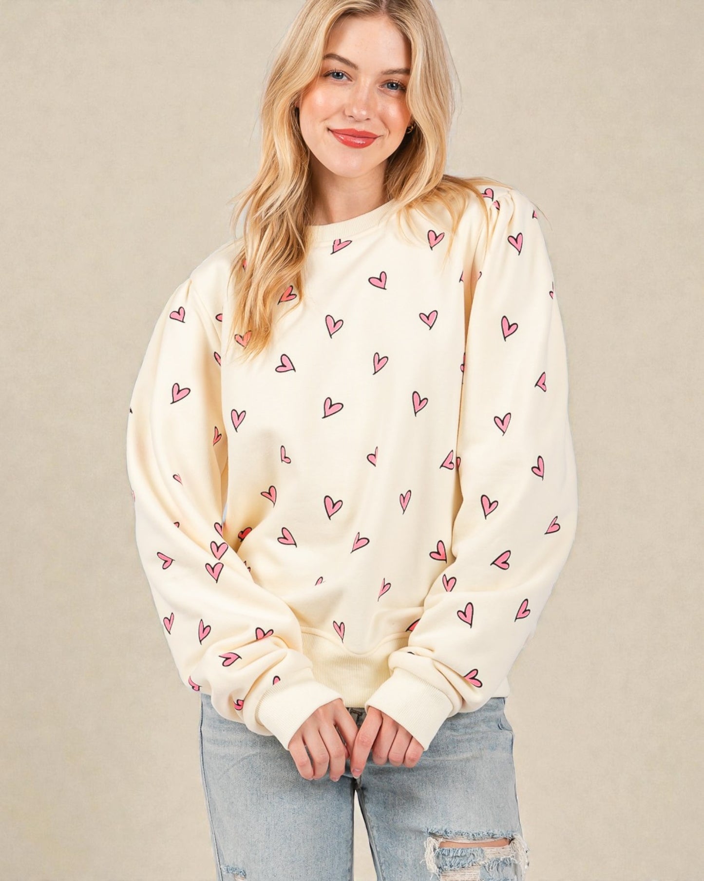 Woman wearing a cream sweatshirt with heart patterns against a beige background