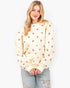 A woman modeling a cream-colored crewneck sweatshirt with a repeating pattern of small pink hearts, paired with light-wash distressed jeans, against a plain white background.