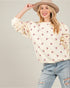 Woman wearing a cream sweater with pink heart patterns and light blue jeans against a plain background