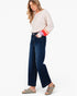 A woman modeling dark blue wide-leg cropped jeans with a cream long-sleeve top and beige slide sandals, standing against a plain white studio background.