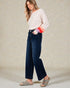 Woman wearing a white sweater with colorful sleeves and dark blue jeans on a neutral background