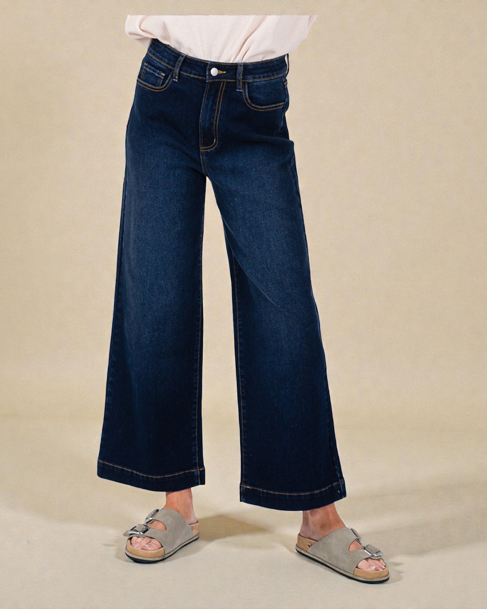 Person wearing dark blue wide-leg jeans on a beige background