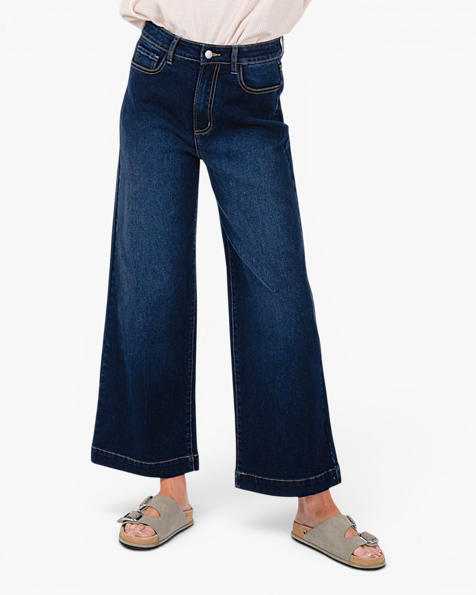 A person wearing dark blue wide-leg cropped jeans with a light-colored top and taupe slide sandals, shown from the waist down against a plain white background.
