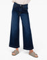 A person wearing dark blue wide-leg cropped jeans with a light-colored top and taupe slide sandals, shown from the waist down against a plain white background.