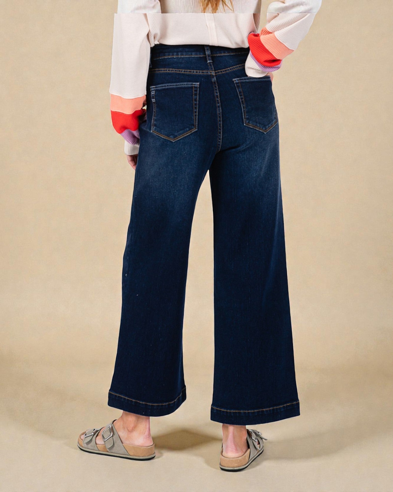 Person wearing dark blue wide-leg jeans on a beige background