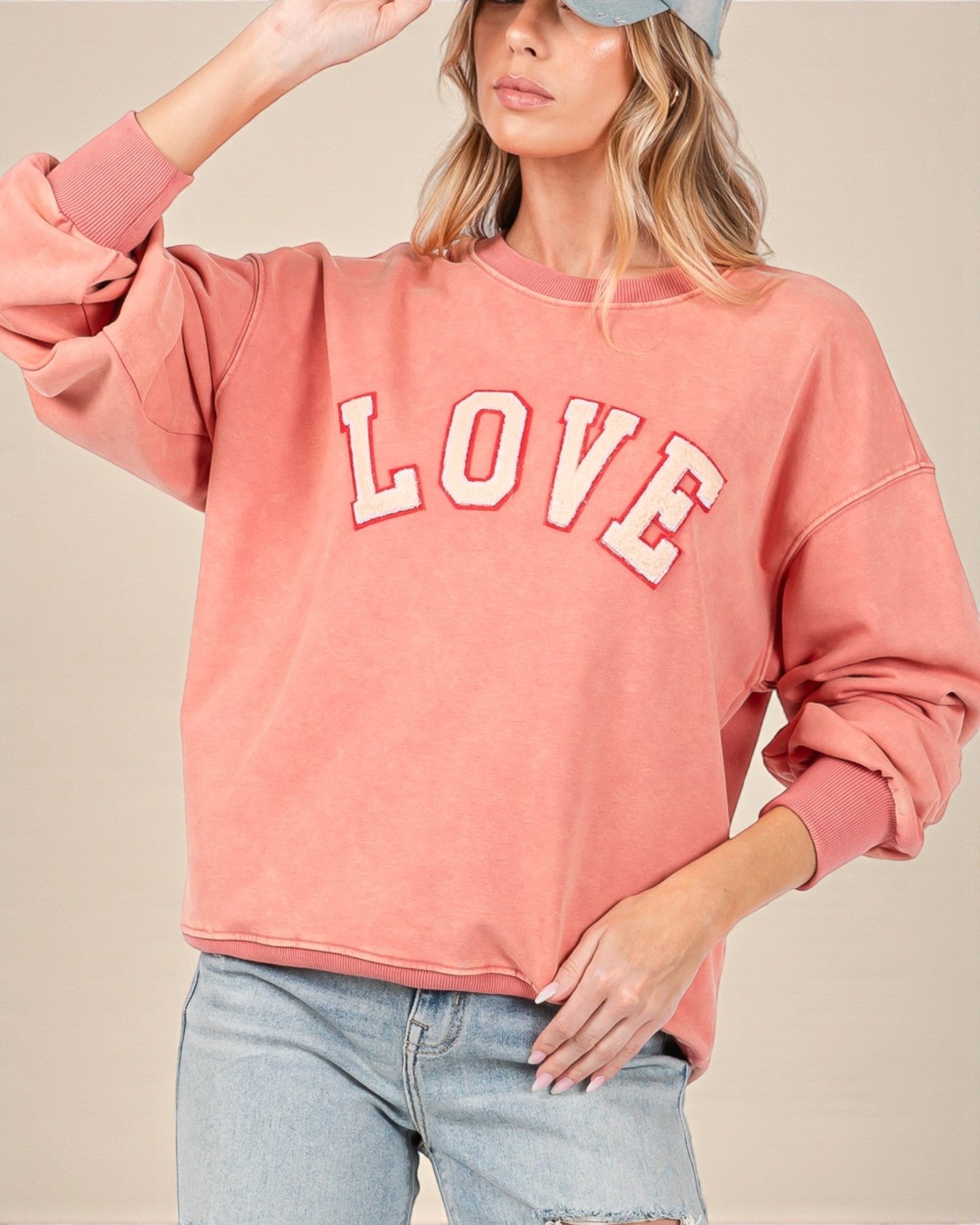Person wearing a pink sweatshirt with 'LOVE' printed on it against a beige background