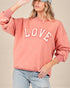 Person wearing a pink sweatshirt with 'LOVE' printed on it against a beige background