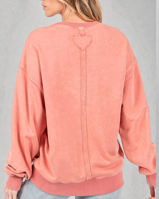 Person wearing a pink sweatshirt with a heart design on the back against a gray background