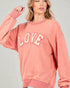 Person wearing a pink 'LOVE' sweatshirt against a gray background