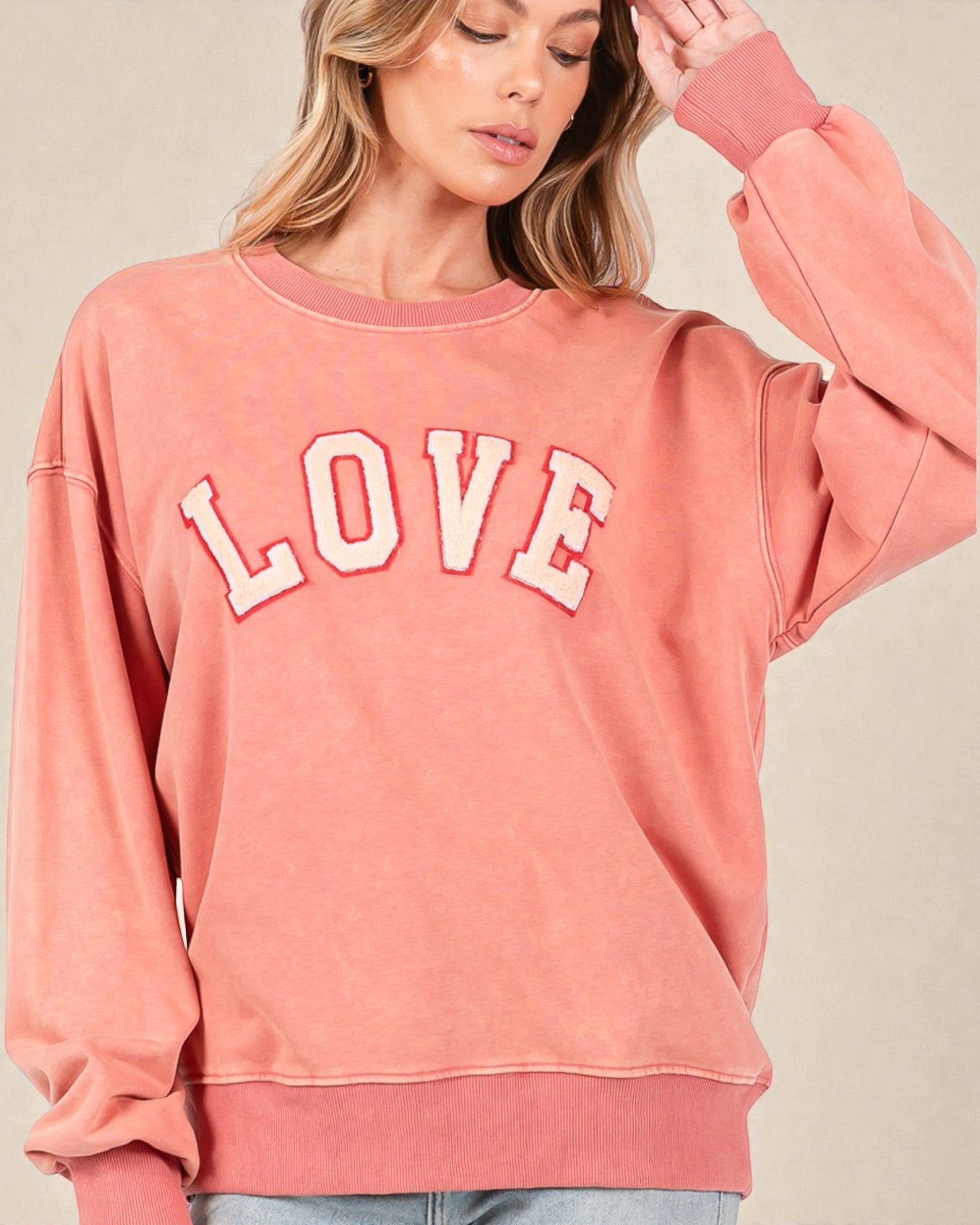 Person wearing a pink sweatshirt with 'LOVE' printed on it against a beige background