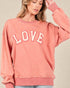 Person wearing a pink sweatshirt with 'LOVE' printed on it against a beige background