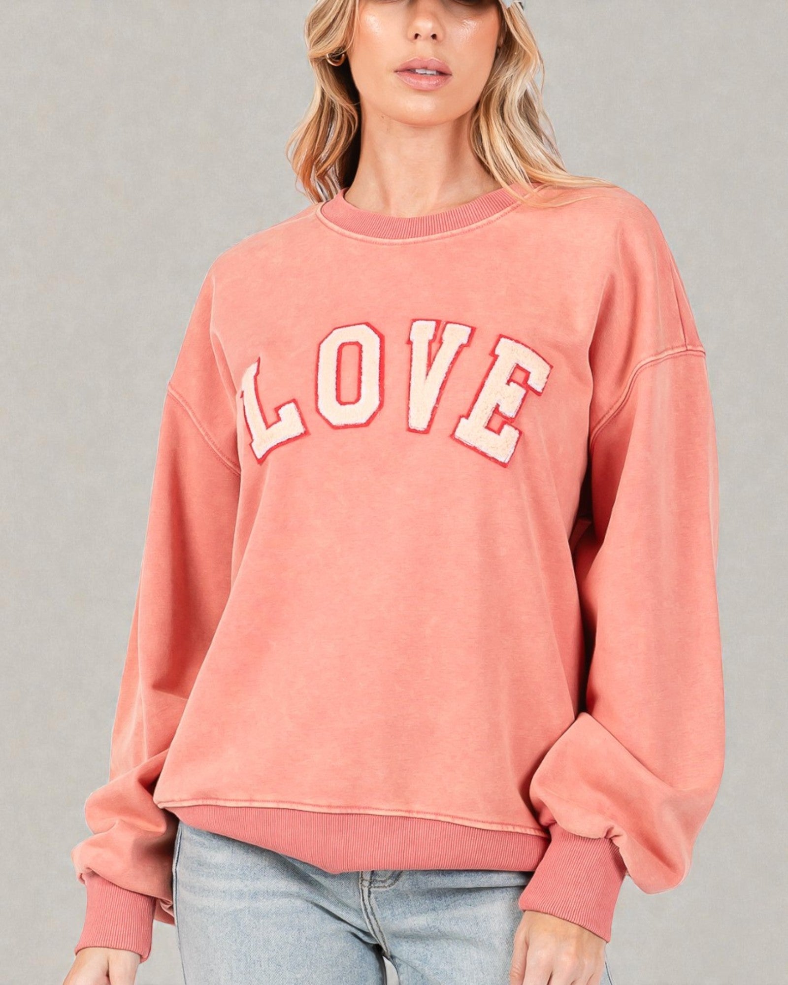 Person wearing a pink 'LOVE' sweatshirt against a gray background