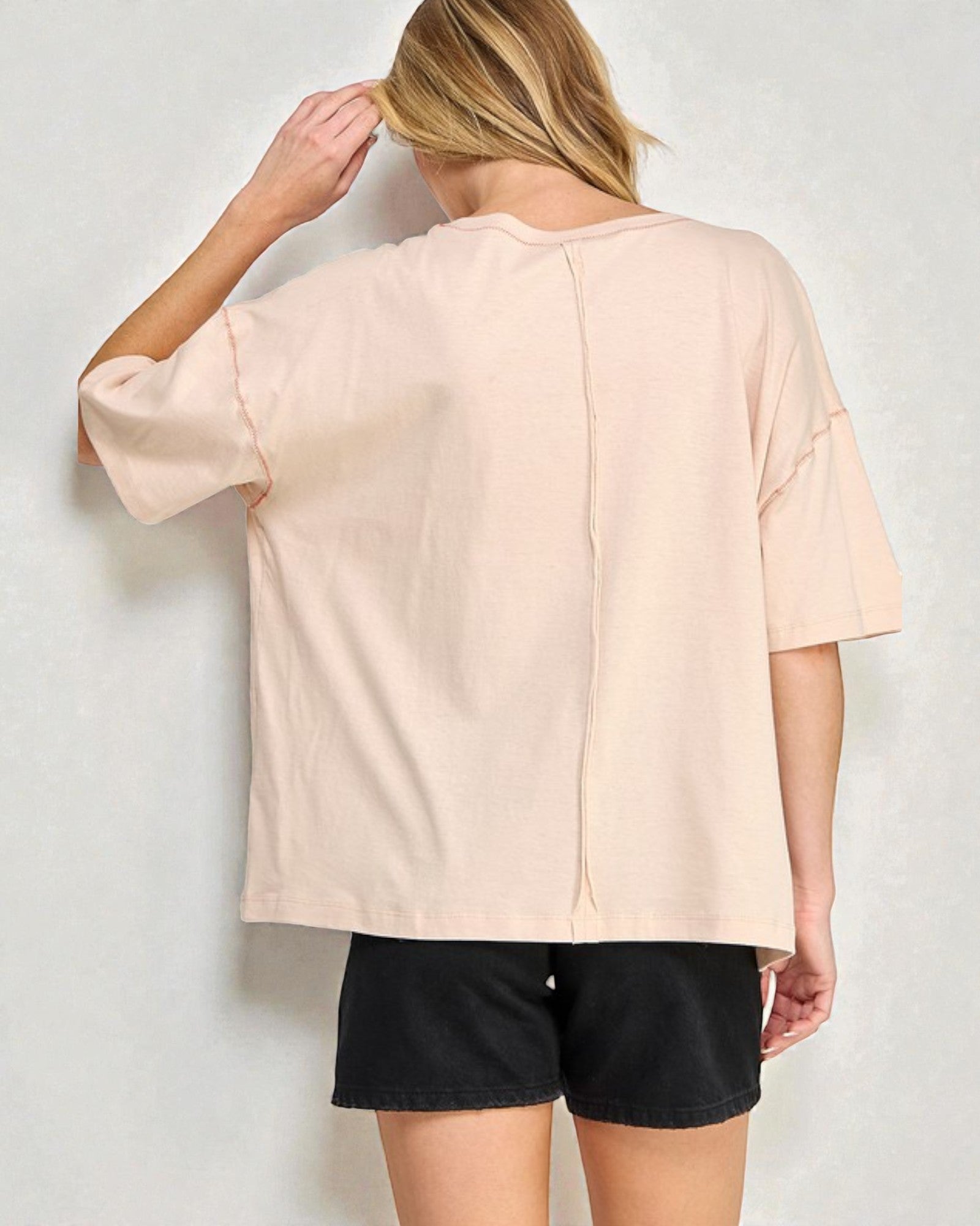 Person wearing a beige oversized shirt and black shorts against a white background