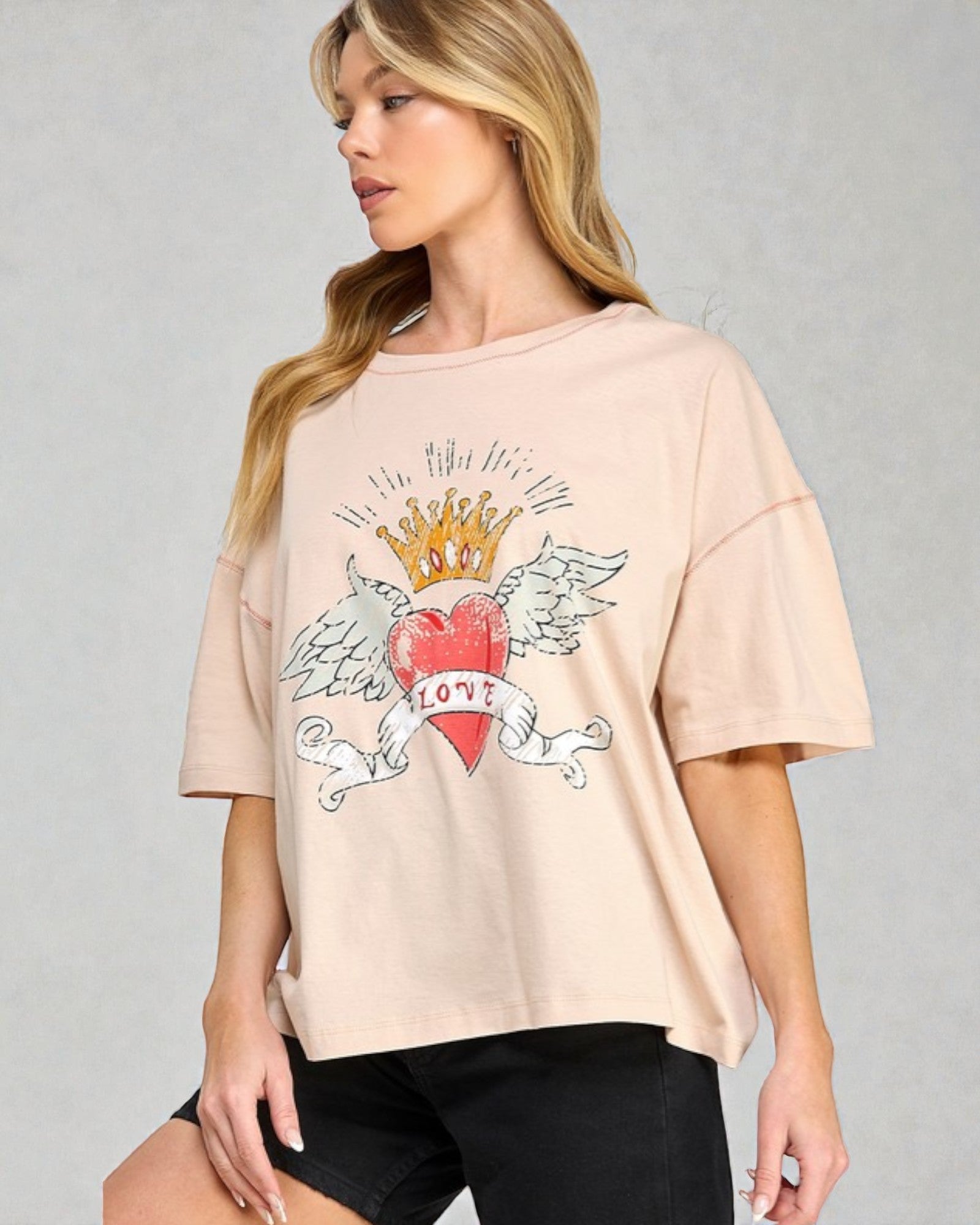 Woman wearing a beige t-shirt with a heart and crown design on a gray background