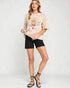 Woman wearing a beige t-shirt with a graphic design and black shorts on a white background