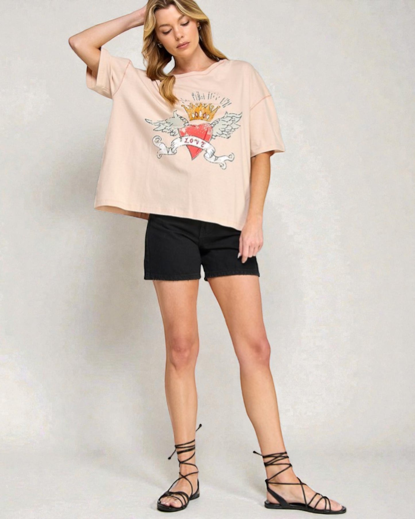 Woman wearing a beige t-shirt with a graphic design and black shorts on a plain background