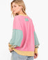 A woman shown from the back wearing a pastel color-block sweatshirt with pink, mint green, and mustard yellow panels, paired with light-wash jeans against a plain white background.