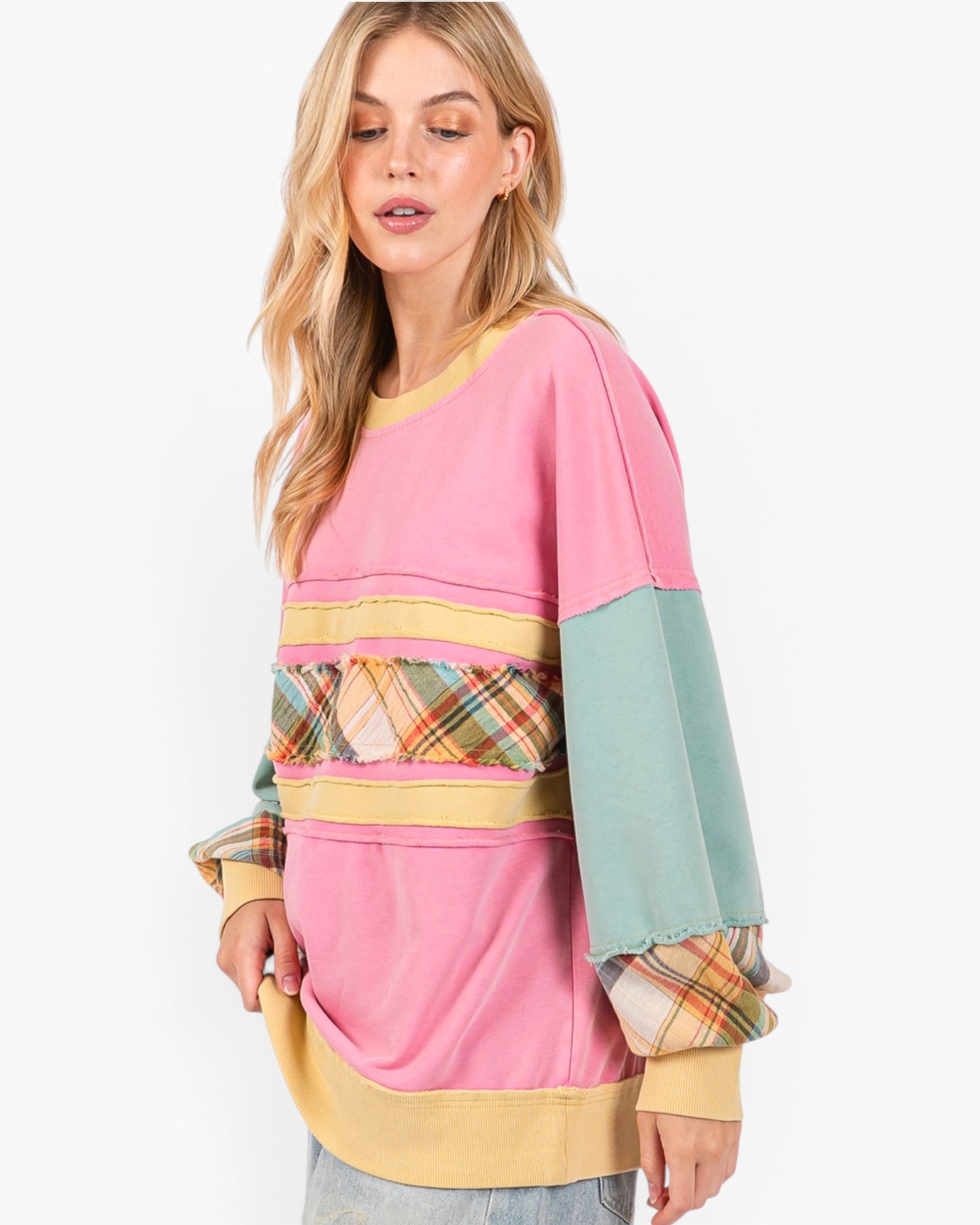 A woman modeling a pastel color-block sweatshirt with pink, yellow, and mint green panels, plaid pattern details, and a crew neck, set against a plain white background.