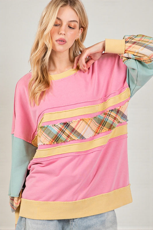 Woman wearing a colorful sweater with pink, yellow, and plaid patterns on a plain background