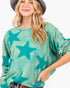 A woman wearing a teal and mint green star-patterned long-sleeve top, styled with a dark gray wide-brim hat and jeans against a plain white background.