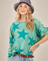 Woman wearing a teal star-patterned shirt with a gray hat on a beige background