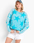 A woman wearing a light blue long-sleeve sweatshirt with a darker blue star pattern, paired with white shorts and a denim cap, against a plain white background.