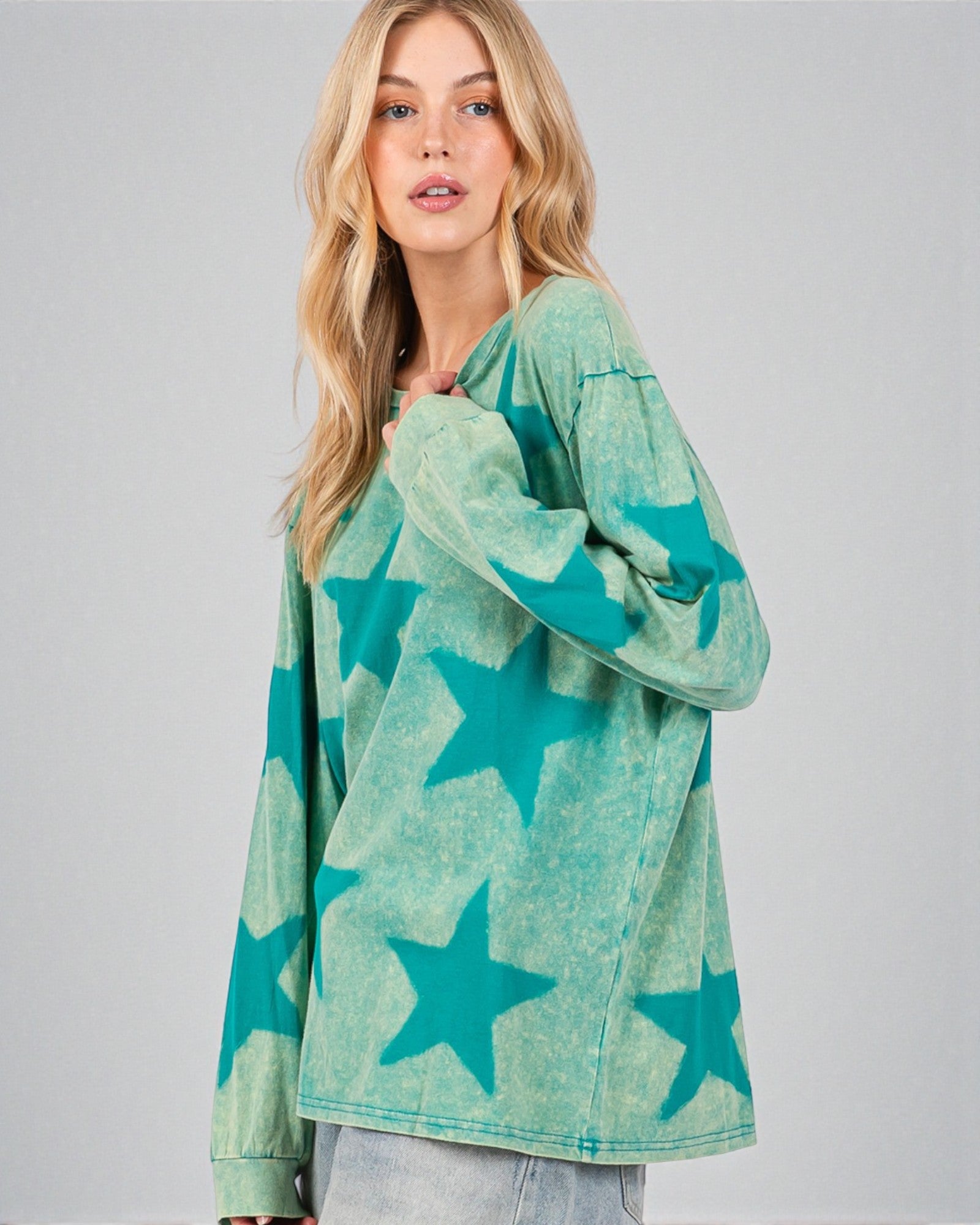 Woman wearing a green oversized sweater with star patterns on a plain background